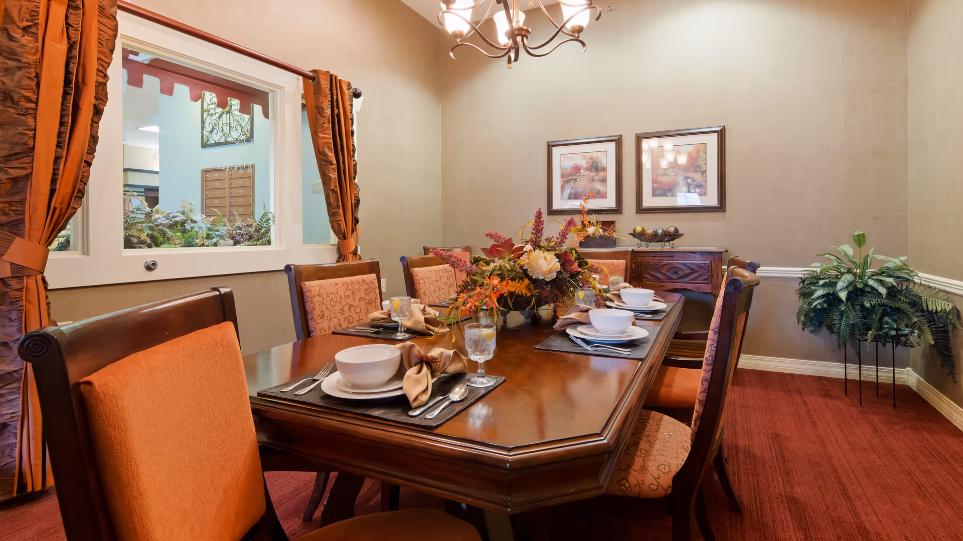 A formal dining room with a set wooden table, floral centerpiece, chandelier, and upholstered chairs.