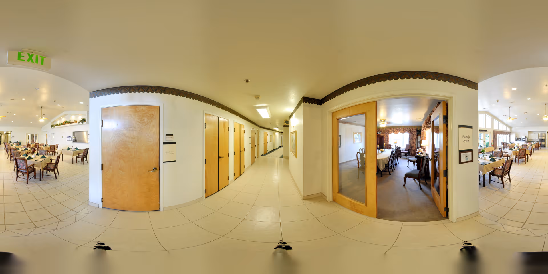 Panoramic interior showing a central corridor flanked by dining rooms with tables and chairs in a senior living facility.