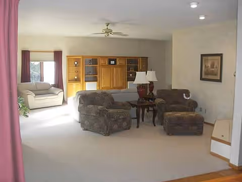 Spacious Cypress Manor living room featuring brown couches, lamps, built-in cabinets, and a ceiling fan.