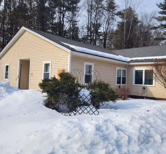 A single-story beige building with snow-covered ground and shrubs in front.
