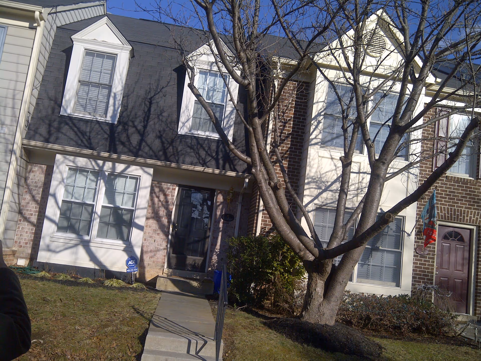 Front exterior of a two-story townhouse-style building with a leafless tree and a walkway leading to the entrance.