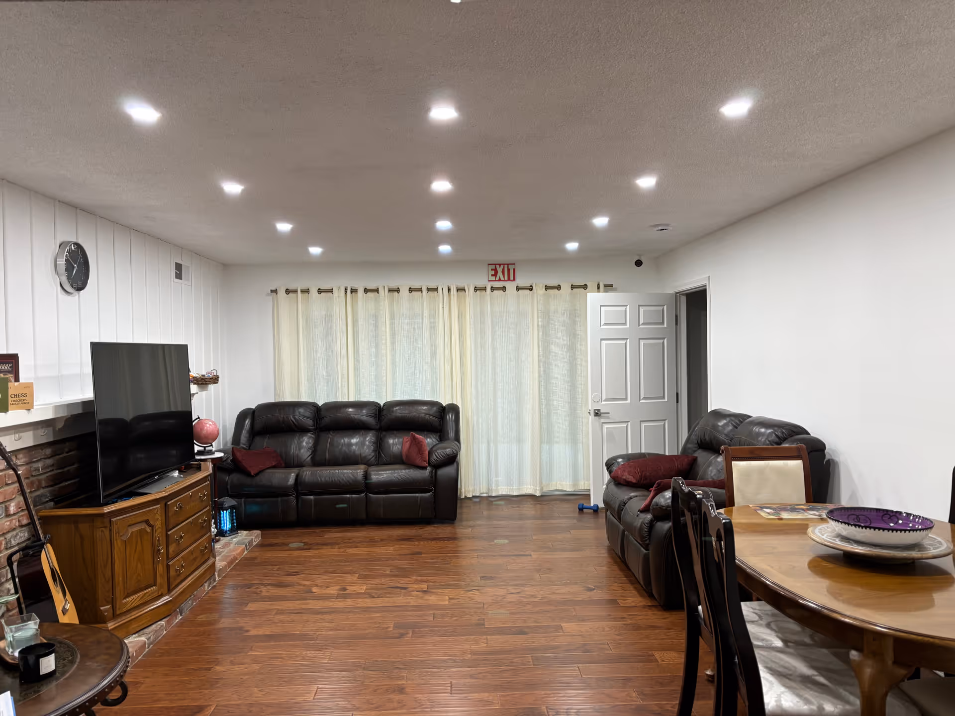 A cozy living room with two leather couches, a television cabinet, and a dining table.
