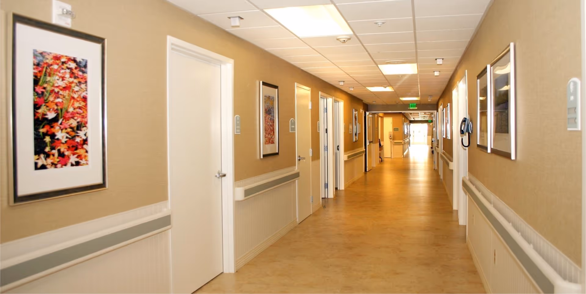 Well-lit interior hallway with doors, handrails, and framed artwork along the walls.
