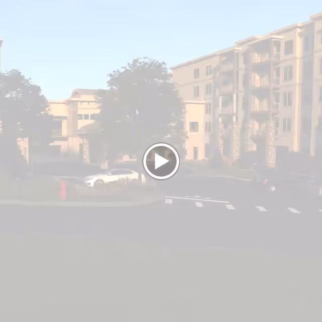 Exterior view of a multi-story senior living facility named Aberdeen Ridge, showing the building's facade, balconies, palm trees, parked cars, and a roundabout with landscaping in front.