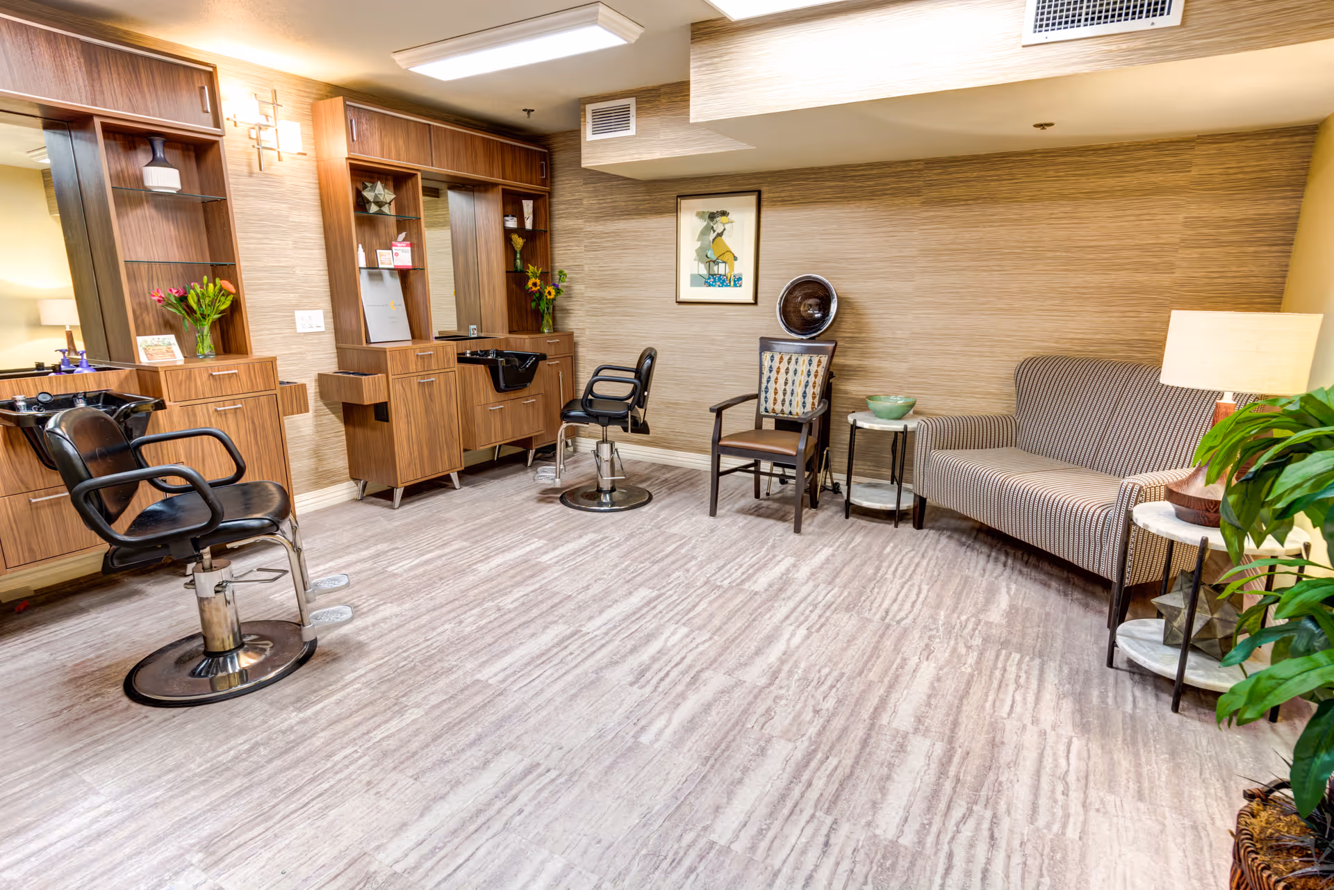 Well-lit interior salon area with styling chairs and wash stations, wooden cabinetry, and a small seating area with a sofa and plants.