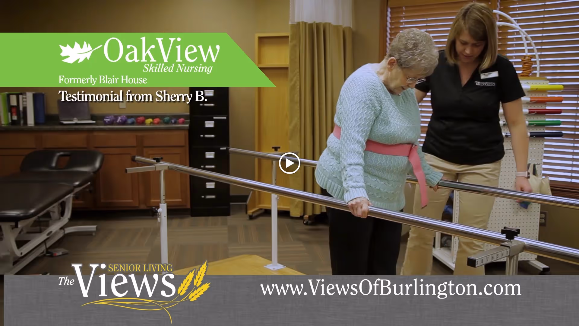 An elderly woman wearing a light blue sweater and black pants is using parallel bars for physical therapy assistance, supported by a female therapist in a black shirt and beige pants in a rehabilitation room.