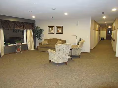 Cozy lounge in a senior facility with sofa, chairs, plants, and a hallway.