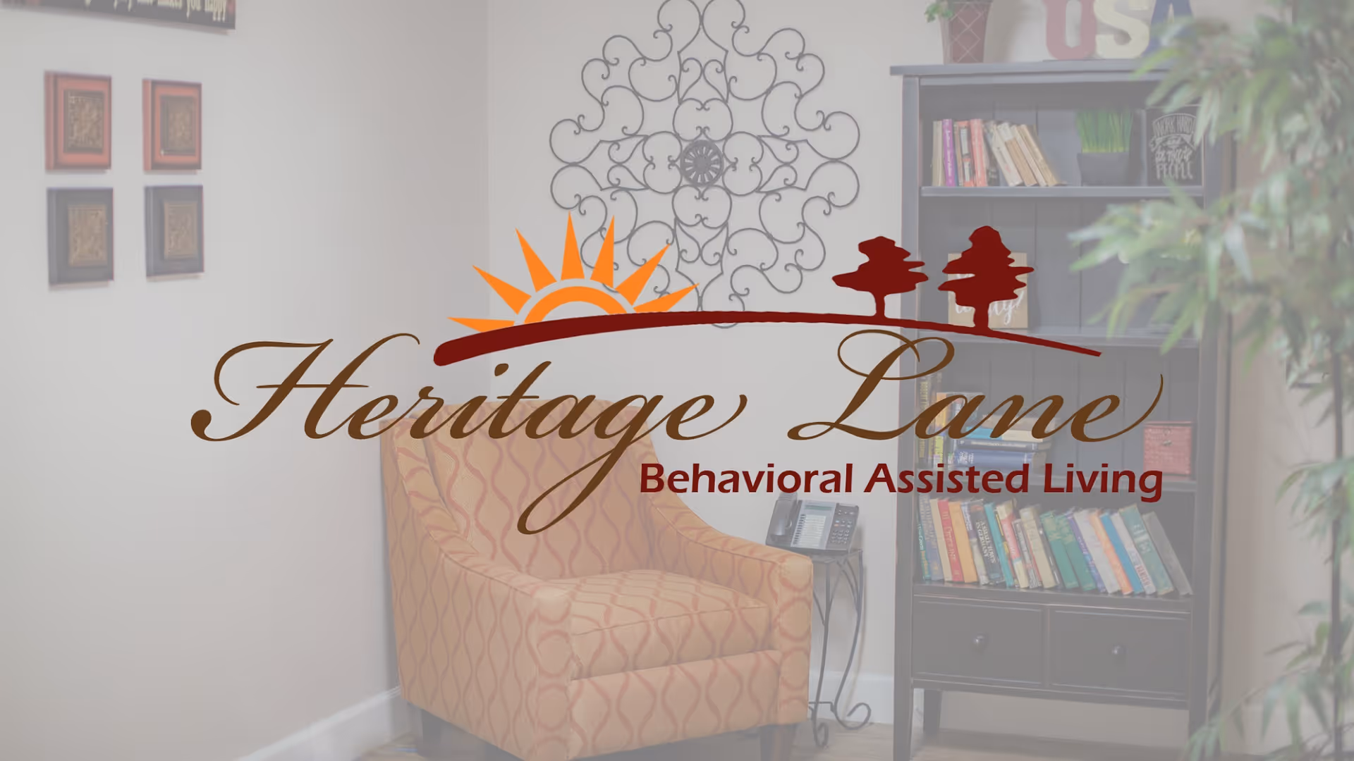 A cozy corner of a living room with a patterned armchair, a small side table with a telephone, a bookshelf filled with books, decorative wall art, and a potted plant.