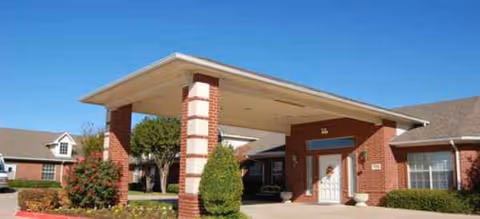 Brick senior living facility with a covered entrance and manicured landscaping.