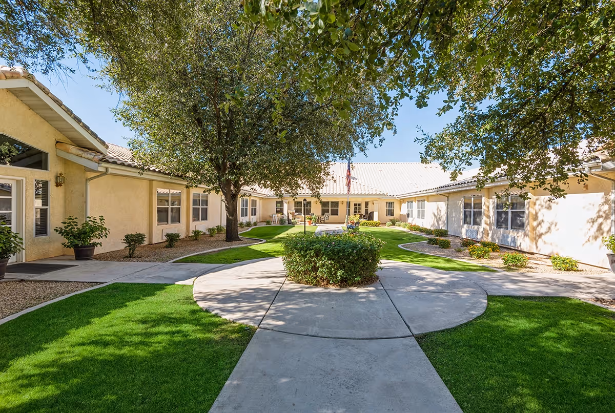 Sunny landscaped central courtyard with a circular concrete walkway, green lawn, trees and a surrounding single-story building.