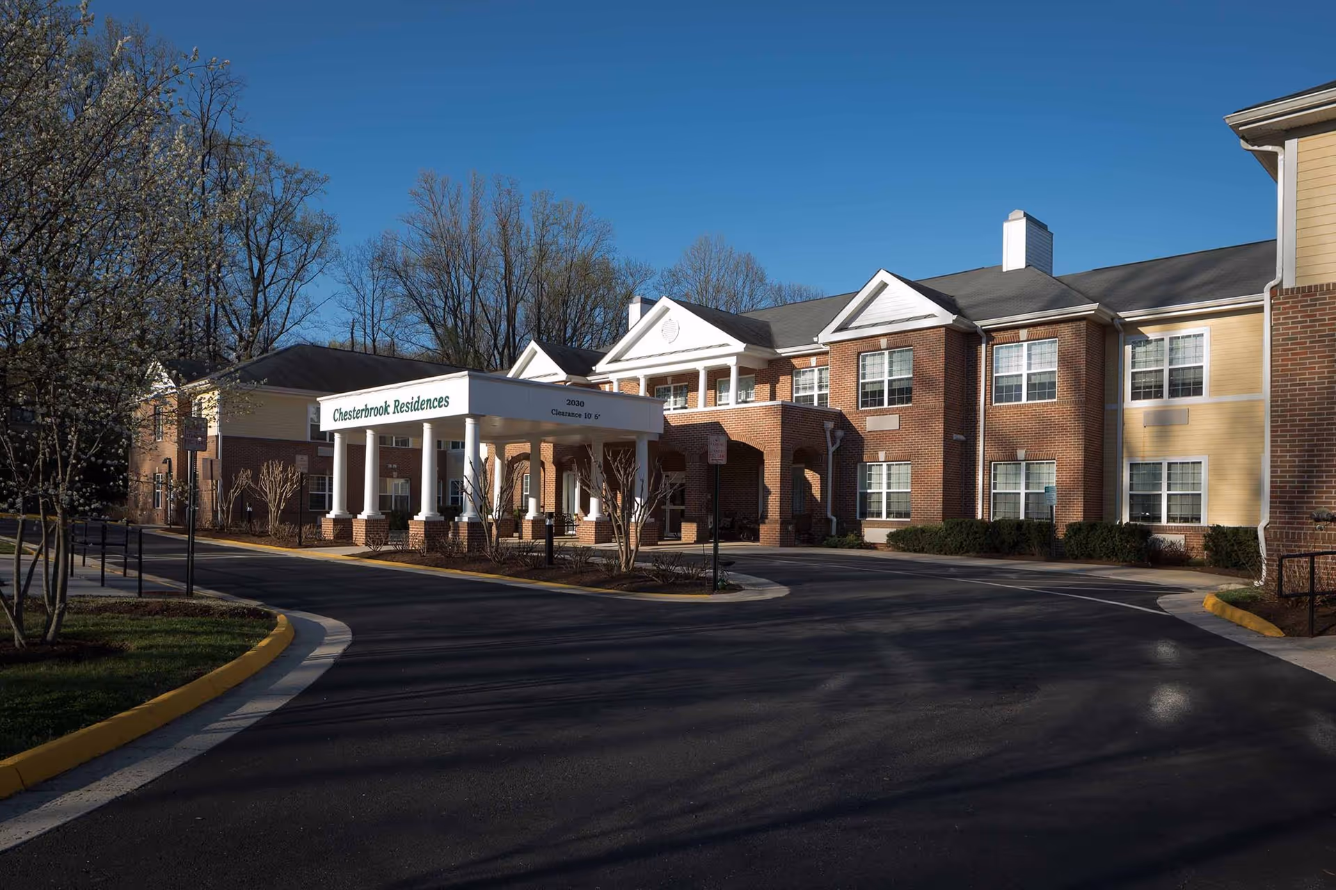 Driveway and entrance of a brick senior living building with a white columned porte-cochere labeled "Chesterbrook Residences".