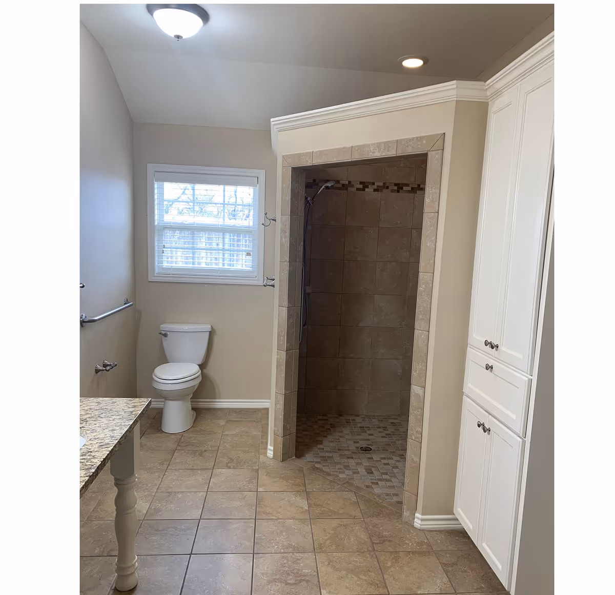 Tile-floored bathroom with a walk-in tiled shower, toilet, vanity countertop and tall white storage cabinets.