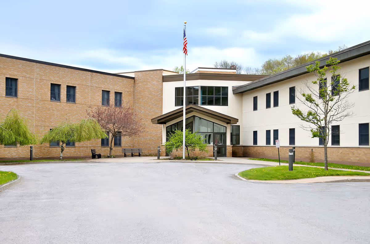 Front entrance of a two-story rehabilitation and nursing center with a flagpole and circular driveway.