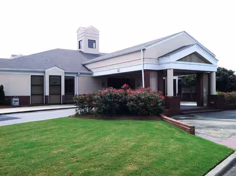 Front view of Wesley Gardens senior living facility with a green lawn and covered entrance.