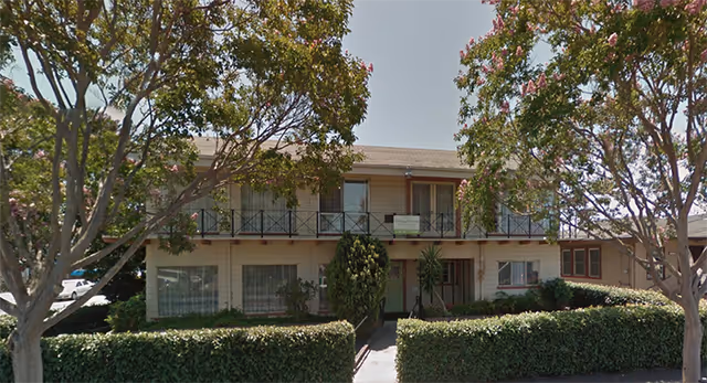 Heritage Haven: two-story beige senior living facility with balconies, shrubs, and flowering trees.