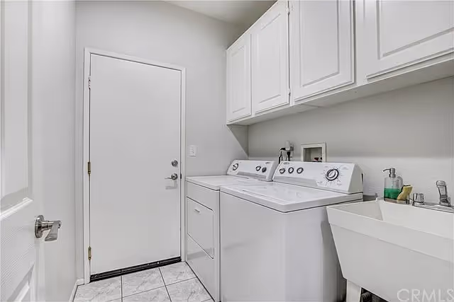 Bright laundry room with a washer and dryer, utility sink, overhead cabinets, and a closed door.