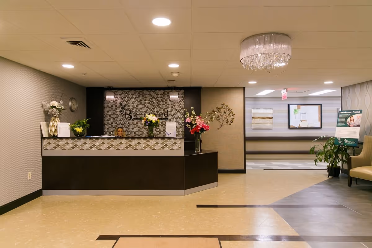 Reception lobby with a front desk, floral arrangements, a chandelier and a hallway in a healthcare facility.