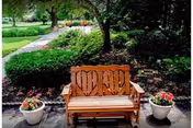 Wooden bench flanked by two flower pots on a paved spot in a landscaped garden with walking paths and trees.