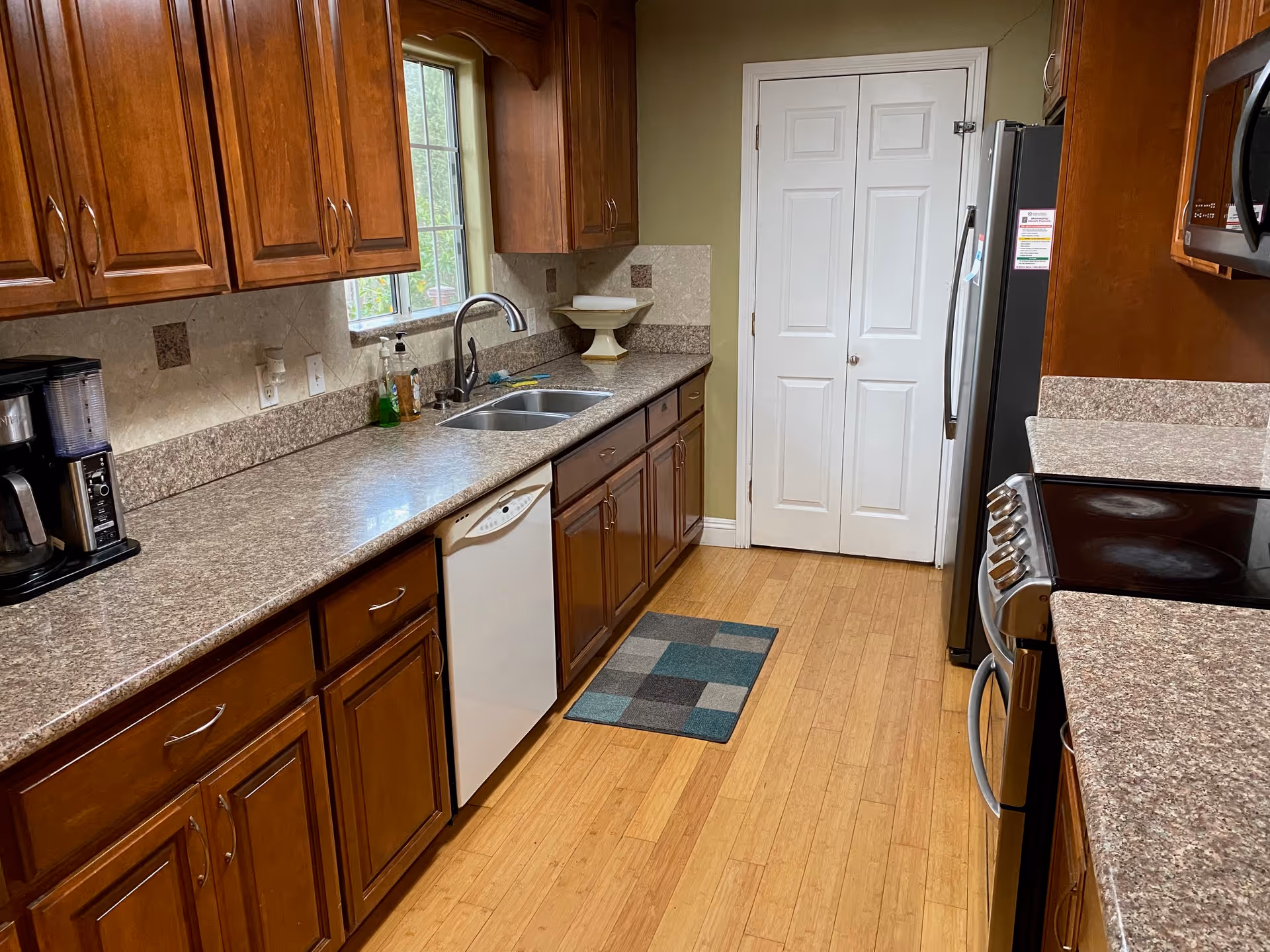 Long kitchen with wooden cabinets, granite countertops, stainless appliances, and a central sink.
