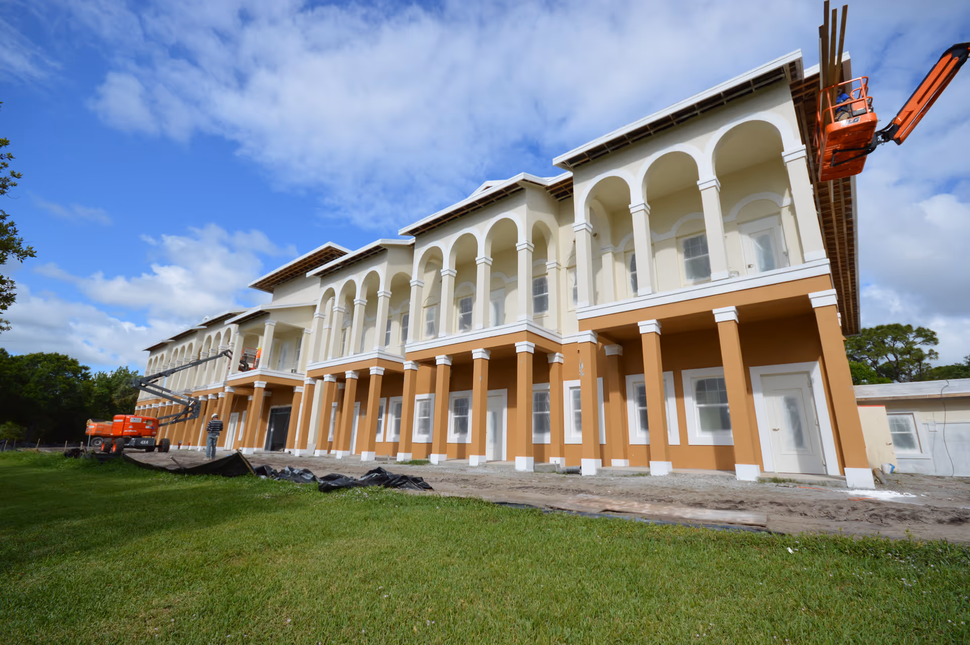 Front exterior of a multi-story Mediterranean-style building with arches and columns under construction.