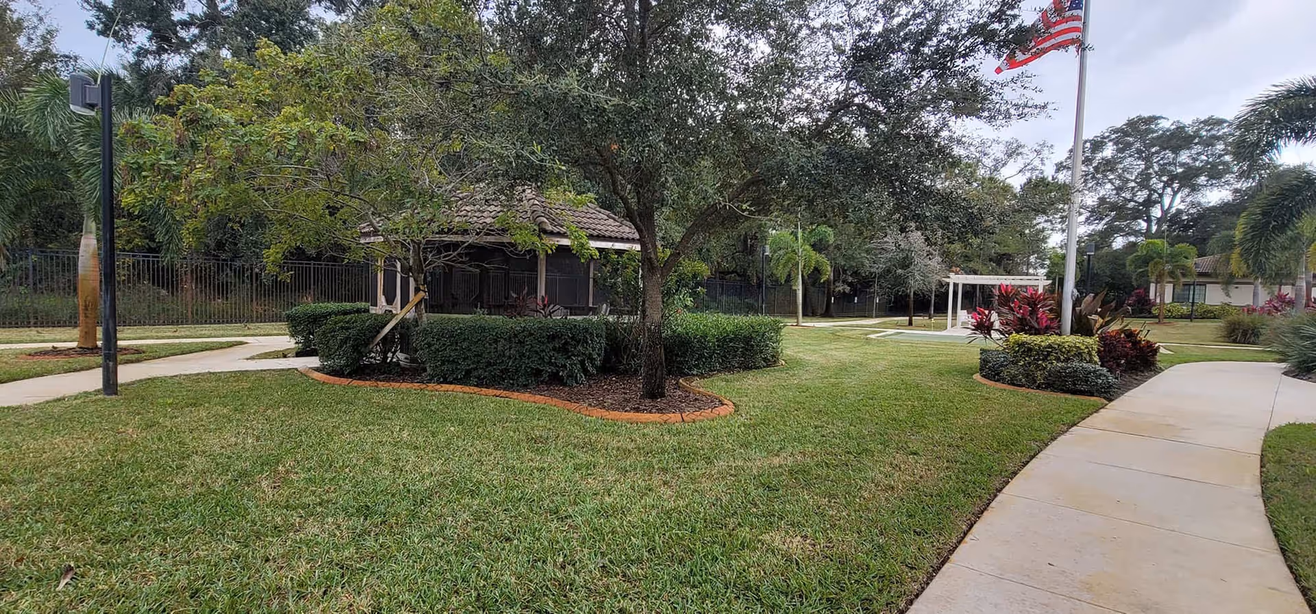 Well-maintained outdoor courtyard with paved walkways, lawn, trees, a gazebo, and a flagpole.