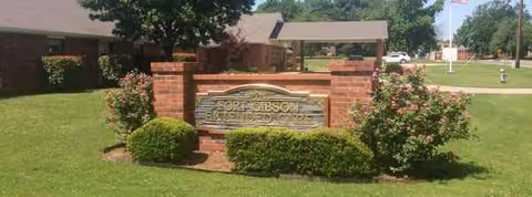 Brick sign reading Fort Gibson Nursing Home on a landscaped front lawn.