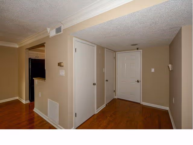 Interior entry hallway with three white doors, beige walls, crown molding, and hardwood floors.