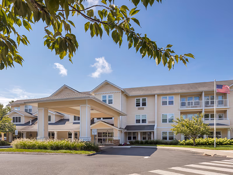 Exterior view of a senior living facility with a covered entrance and American flag.