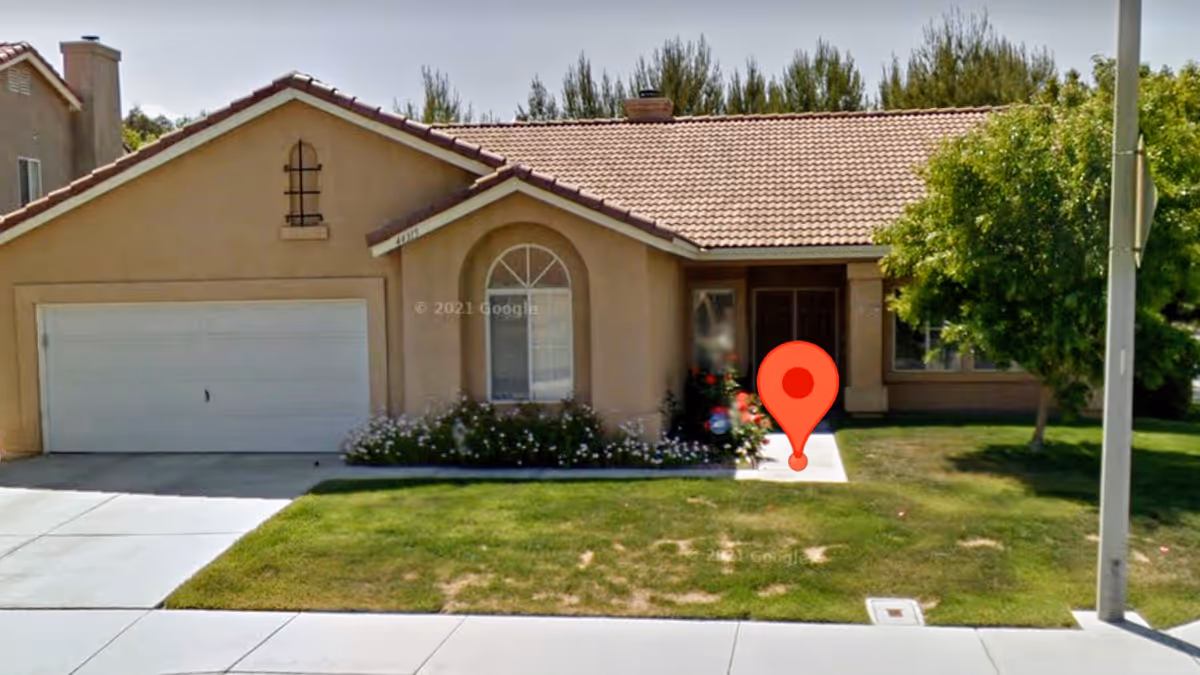 Front exterior of a beige single-story house with a two-car garage, lawn, and a red map marker on the walkway.