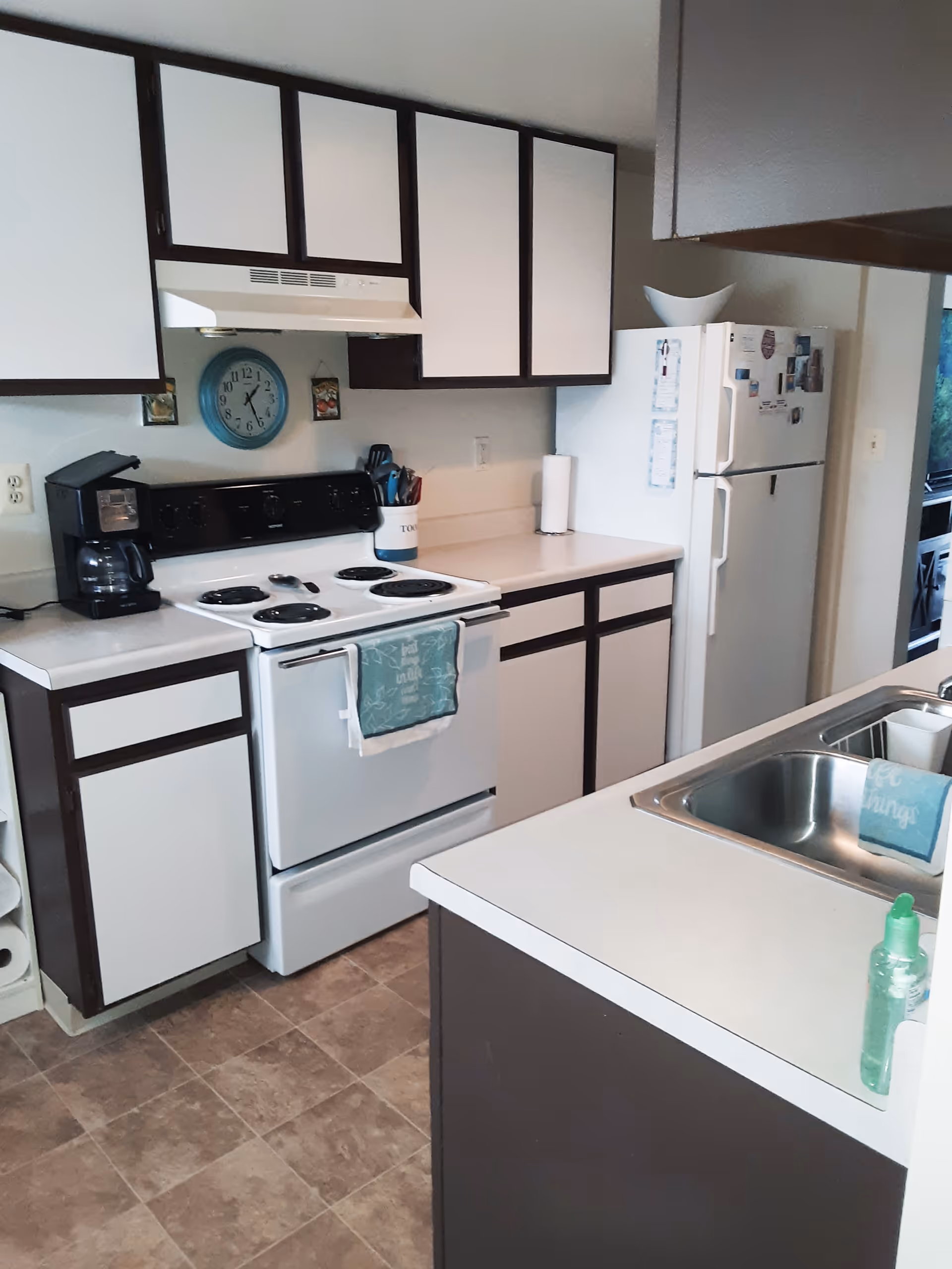 Compact kitchen with white cabinets, an electric stove, refrigerator, and a sink in a countertop island.