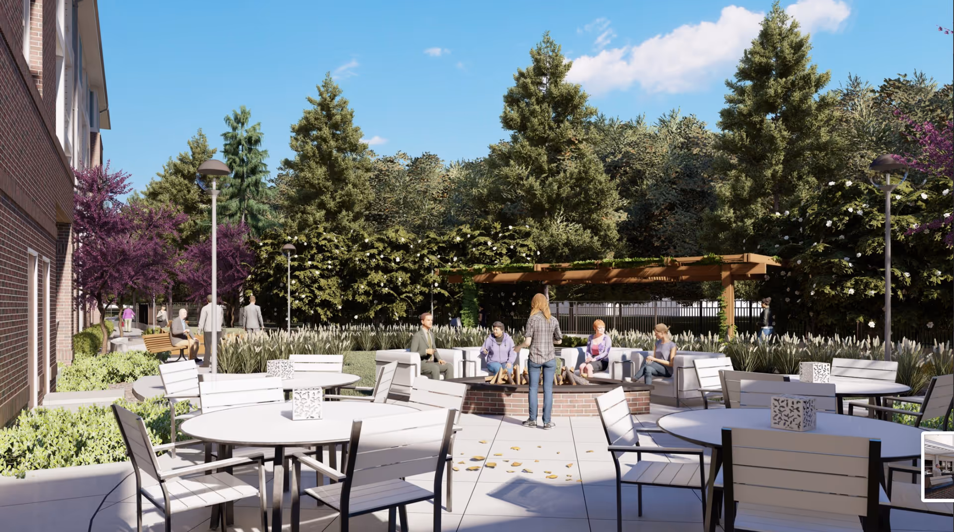 Outdoor patio area at Acclaim at Cary Pointe with round tables and chairs, a fire pit surrounded by seating, several people sitting and standing, lush greenery, trees, and a pergola in the background under a clear blue sky.