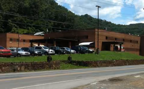 Exterior view of Welch Community Hospital: brick building with parked cars and green hillside.