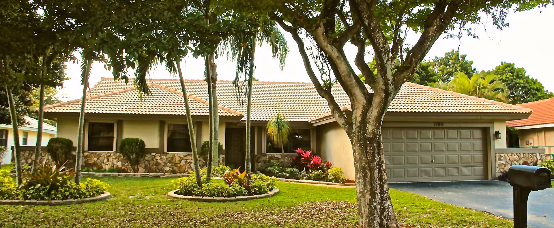 Single-story house with a tiled roof and attached two-car garage, landscaped front yard and trees.