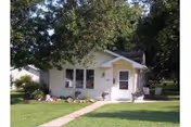 Front view of a small white, single-story building with front entrance, windows, and green lawn.