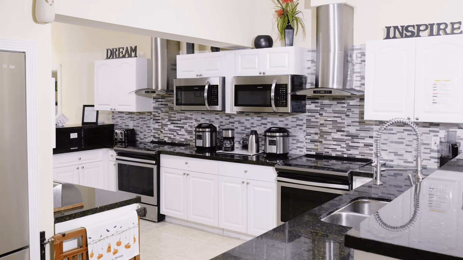 Modern communal kitchen with white cabinets, stainless-steel appliances, black granite countertops, and a gray mosaic tile backsplash.