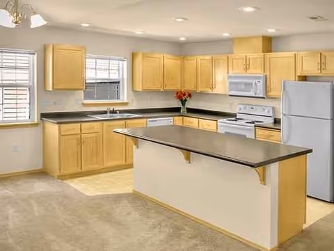 Bright, well-lit senior living kitchen with wooden cabinets, island, and appliances.