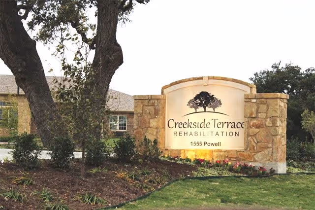 Stone entrance sign reading "Creekside Terrace Rehabilitation 1555 Powell" surrounded by landscaping and trees in front of the facility.