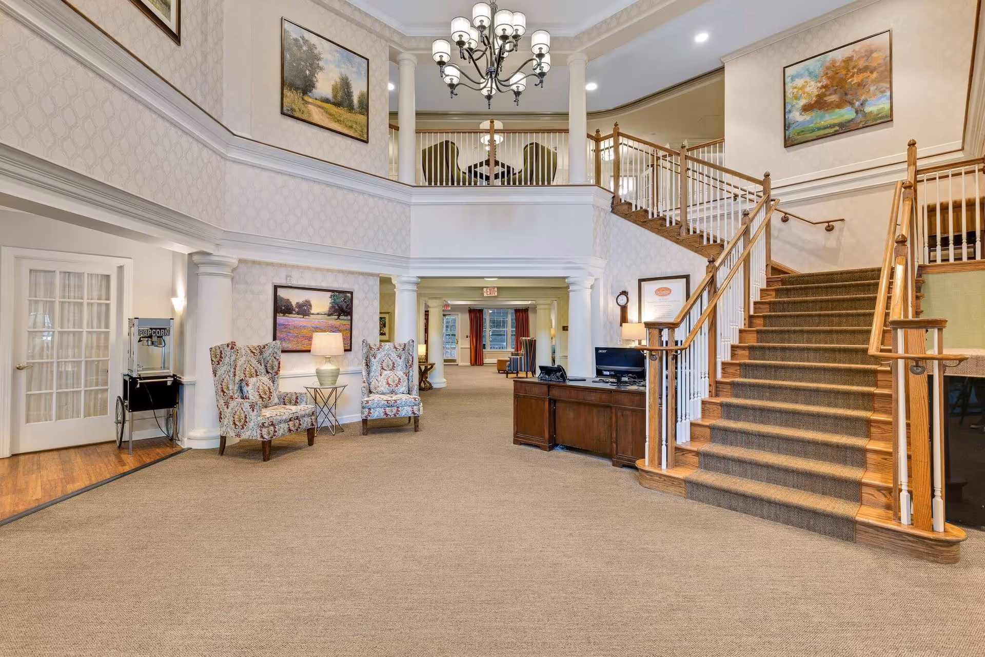 Spacious two-story lobby with carpeted floor, seating area, reception desk, and a staircase leading to an upper balcony.