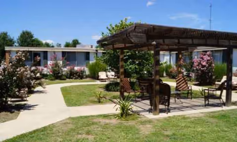 Outdoor courtyard with pergola, seating, and walkways beside a nursing and rehabilitation center.