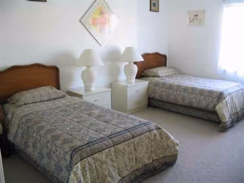 Two single beds with matching quilts and nightstands with lamps in a shared bedroom.