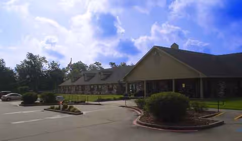 Exterior view of Dogwood Trails Manor with driveway, parking, and landscaped front yard.