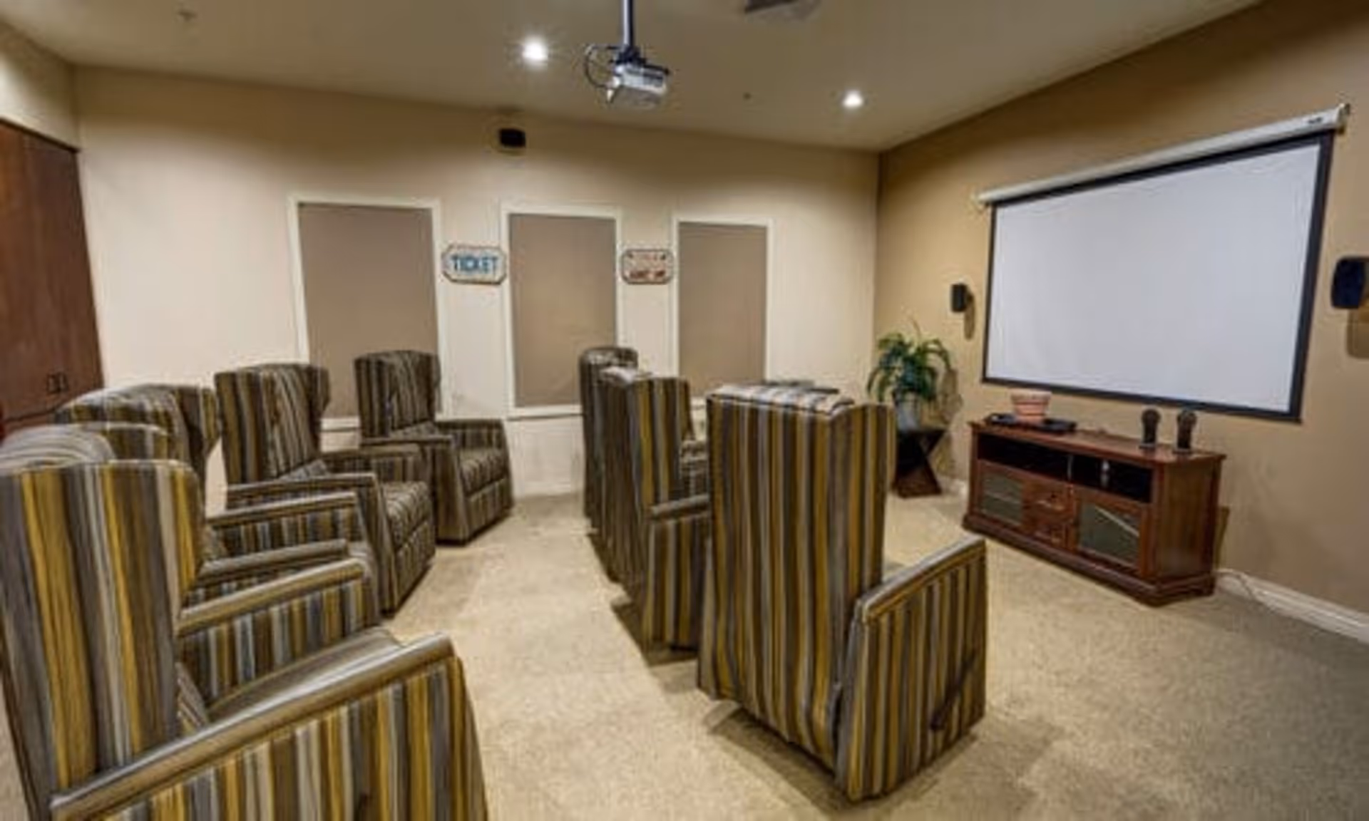 Small screening room with striped armchairs arranged in rows facing a projector screen and media console.
