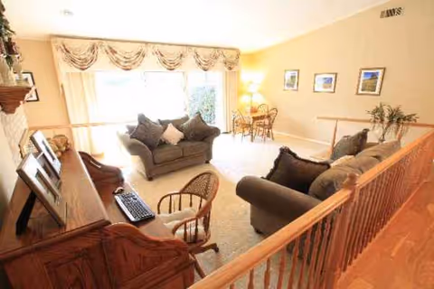 Cozy living room in a residential care facility with sofas, chairs, piano, and large window.