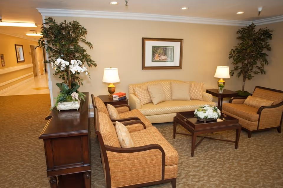 Well-lit common sitting area with a sofa, armchairs, coffee table, lamps, and decorative plants.