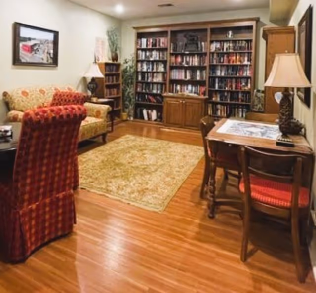 Cozy common room with built-in bookshelves, upholstered chairs and sofa, a rug on hardwood floors, and a small table with lamps.