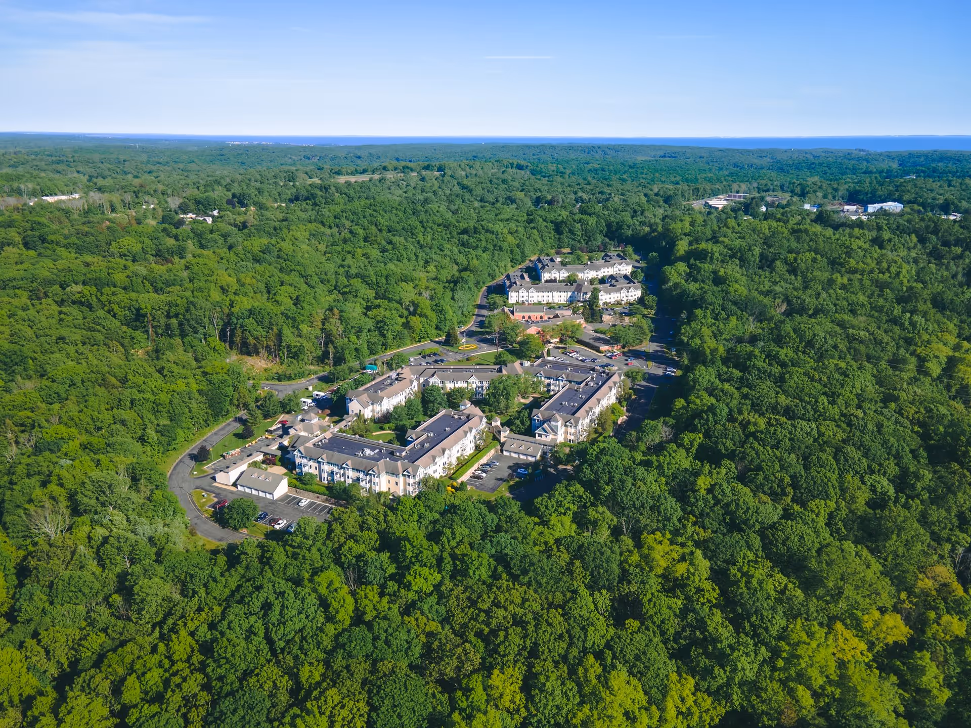 Aerial view of Evergreen Woods senior living facility surrounded by dense green forest under a clear blue sky.