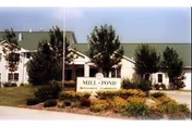 Front exterior of a white building with a green roof, landscaped entrance, and a sign that reads 'MILL POND'.