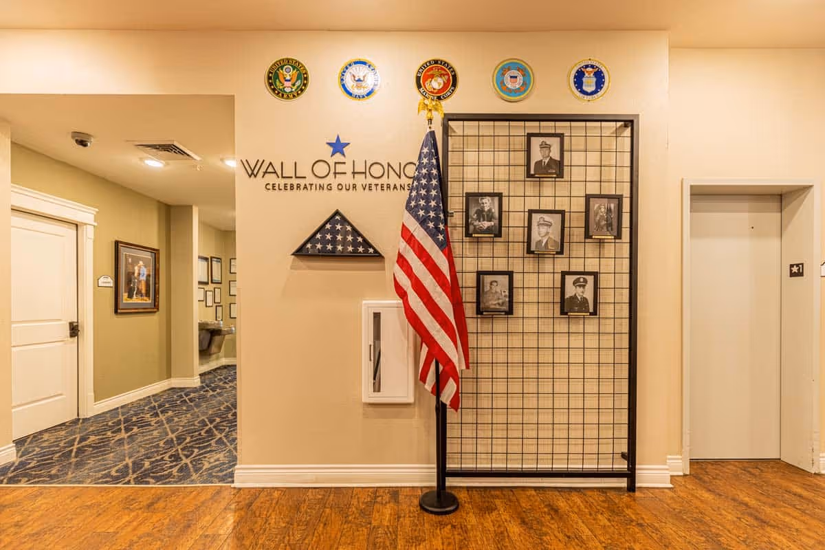 Interior hallway featuring a 'Wall of Honor' display with an American flag, a folded flag case and framed veteran photos.