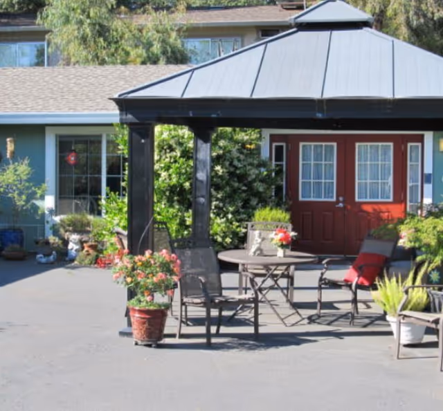 Outdoor courtyard with a gazebo, patio table and chairs, potted plants, and a red double-door entrance to the building.