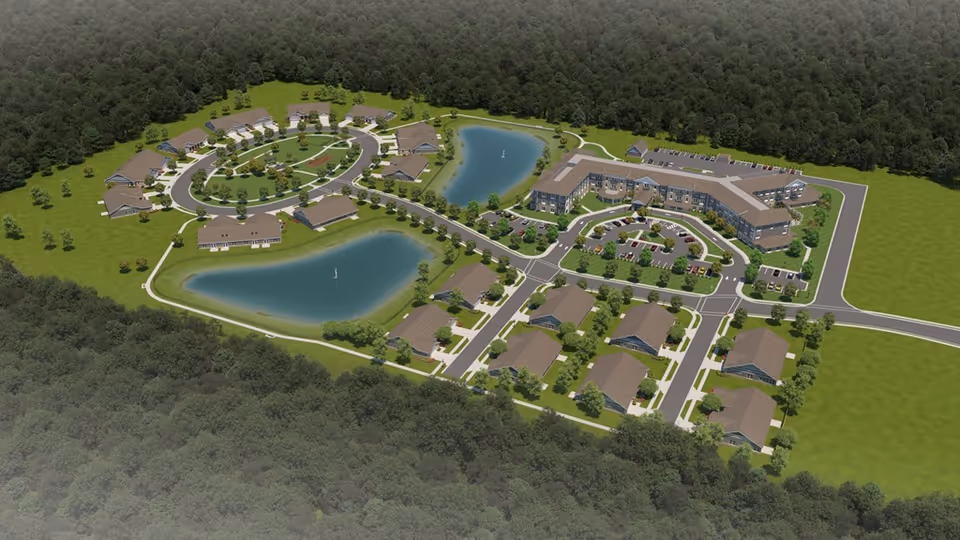 Aerial view of Woodland Terrace of Danville senior living facility showing multiple buildings arranged around two large ponds with fountains, surrounded by green lawns and trees, with roads and parking areas connecting the buildings.